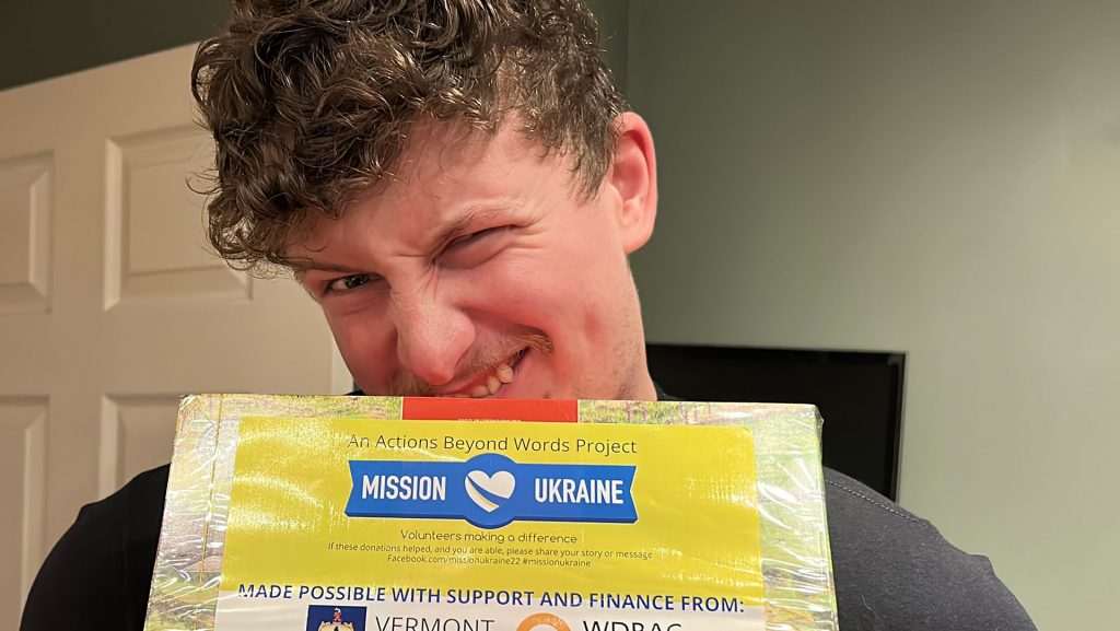 Picture of Nathan Mullaney, working with Actions Beyond Words (ABW) puling a funny face whilst almost eating a humanitarian age package with Mission Ukraine, WDRAC and Vermont labels