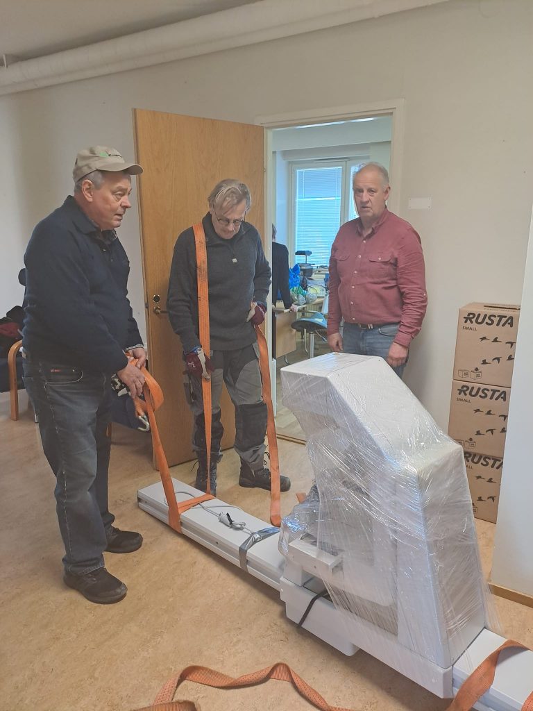 Finland Dentists preparing the - X-ray for shipment to Ukraine - 3 guys with shrink wrap and ratchet straps for lifting.