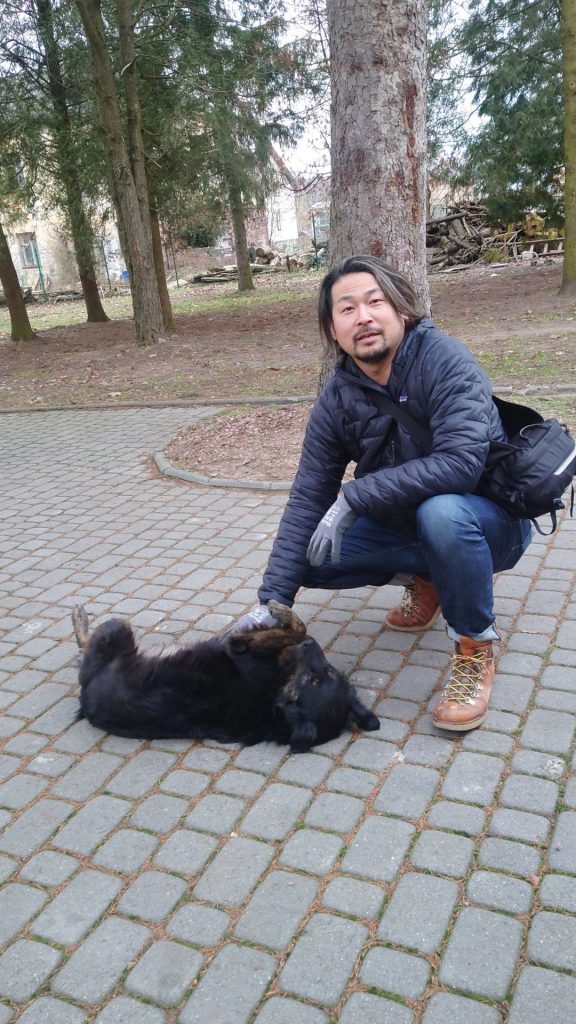 Akira crouching down to pet a friendly black dog that is enjoying being pet on a walkway through a park in Ukraine